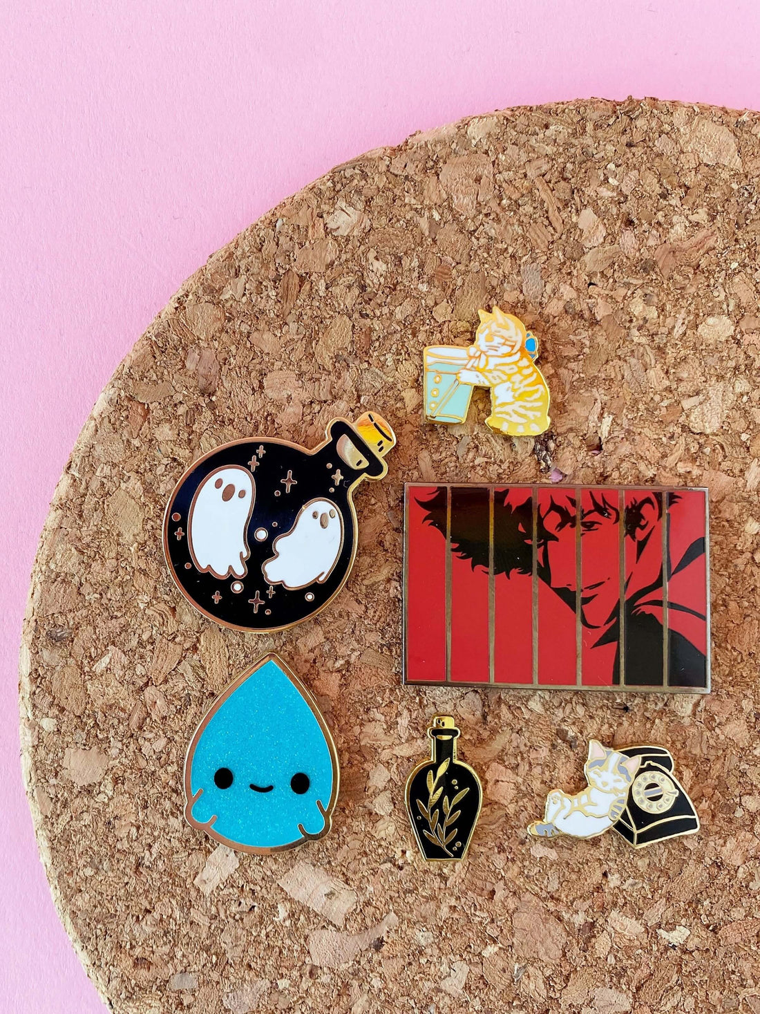 A cork trivet displaying a variety of enamel pins with cats, potions, Spike Spiegel from Cowboy Bebop, and a kawaii raindrop.